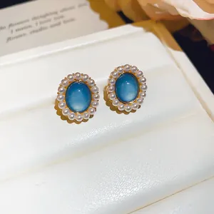 Close-up of elegant oval blue resin stud earrings with white pearl border on white display
