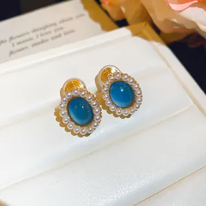 Detail view of oval blue resin stud earrings with delicate pearl border on white display