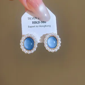 Detail of elegant oval blue resin earrings with pearl trim displayed on a branded card