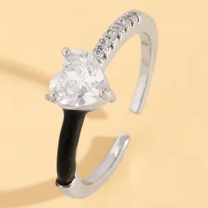 Close-up detail of a silver open ring featuring a clear heart-shaped zircon and black enamel
