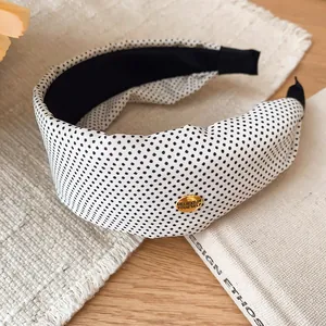 Détail d'un serre-tête vintage en tissu à pois blancs et noirs avec une pièce en métal doré.