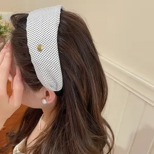 Détail d'un serre-tête rétro en tissu à pois noirs et blancs porté par une femme.