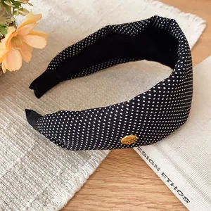 Vue détaillée d'un serre-tête rétro en tissu à pois noir et blanc avec une plaque dorée