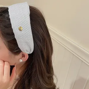 Détail d'un serre-tête rétro en tissu à pois noirs et blancs sur les cheveux du modèle