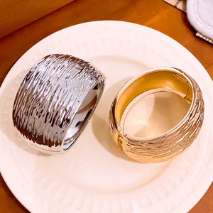 Detailed close-up of wide metal bangles featuring unique crinkle texture in gold and silver