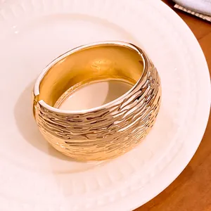 Close-up of a luxury gold-tone bangle with a distinctive rippled texture on a plate