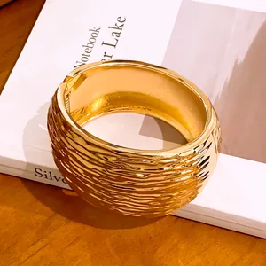 Detailed close-up of golden wide bangle featuring unique wrinkled texture and hinge closure