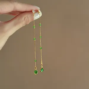 Detailansicht langer goldener Quastenohrringe mit leuchtend grünen Zirkonsteinen und Perlen