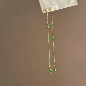 Nahaufnahme eleganter langer goldener Quastenohrringe mit grünen Kristallen und Zirkonia.