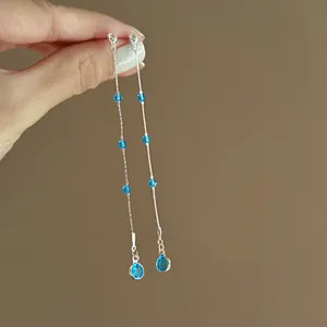 Nahaufnahme eleganter langer Silber-Quastenohrringe, verziert mit leuchtend blauen Zirkonia
