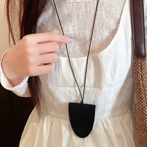Minimalist black leather shield glasses holder necklace worn by model on white dress