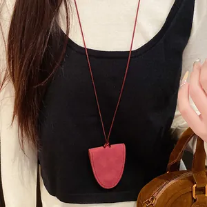 Detail view of a red leather glasses holder necklace worn over a black and white sweater