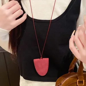 Close-up detail of a minimalist red leather shield pendant necklace on a long cord
