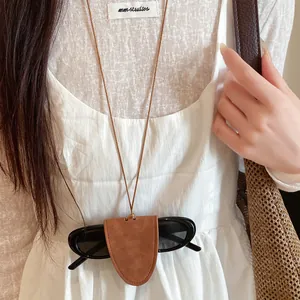 Close-up detail of a minimalist brown leather sunglasses holder necklace on a white dress