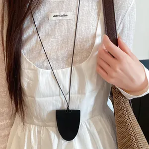 Close-up of a black leather shield pendant eyeglass holder necklace worn on a white dress