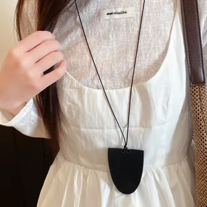 Close-up of a black leather bell pendant on a minimalist long cord necklace worn by a model.