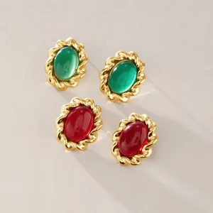 Dettaglio ravvicinato di orecchini a lobo vintage in oro con pietre cabochon ovali verdi e rosse.
