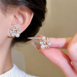 Detail of 18k gold plated zircon star earrings with pearls shown on ear and held by hand