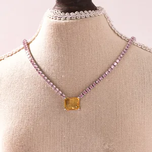 Close-up view of a pink zircon tennis necklace with a central rectangular yellow gemstone pendant.