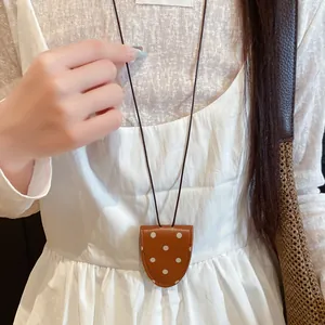 Nahaufnahme einer braunen Lederkette mit Polka-Dots als Brillenhalter zu einem weißen Kleid