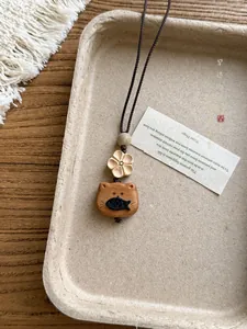 Detailed macro view of a handmade wooden cat and fish pendant necklace on a rustic tray.