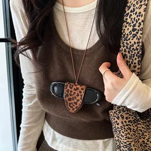Detail view of leopard print leather sunglasses holder necklace worn by a model in a brown sweater.