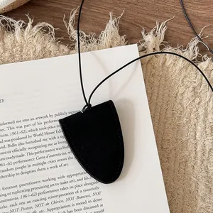 Detail of the minimalist black leather glasses holder necklace on a textured background