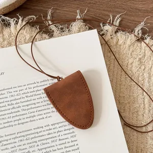 Detail of a minimalist brown leather necklace eyeglass holder on a white book background.