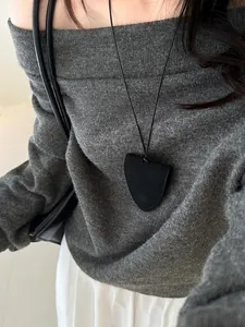Close-up of a minimalist black leather glasses holder necklace on a grey knit sweater