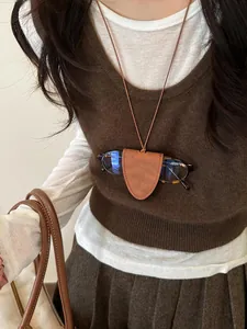 Detailed shot of a stylish leather glasses holder necklace worn over a brown sweater vest