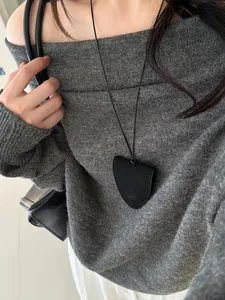 Close-up of a minimalist black leather heart pendant necklace worn over a grey sweater