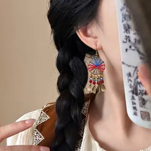 Detailed view of ethnic woven circular earrings with retro leaf charms on a model braid