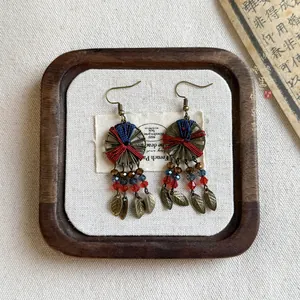 Detail of vintage ethnic woven earrings with red and blue thread and bronze leaf charms
