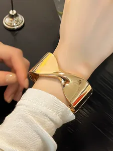 Vista detallada de un elegante brazalete abierto geométrico dorado en la muñeca de una mujer