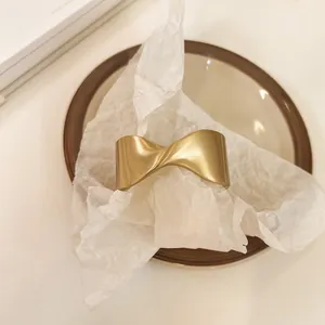 Primer plano de un brazalete geométrico retorcido en oro mate sobre plato de cerámica