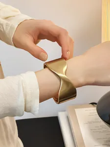 Primer plano de un brazalete cruzado geométrico de oro mate en la muñeca de una mujer