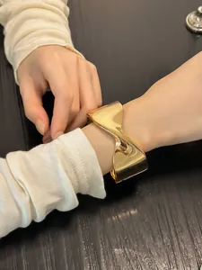 Primer plano de un brazalete dorado geométrico retorcido llevado en una muñeca con manga.