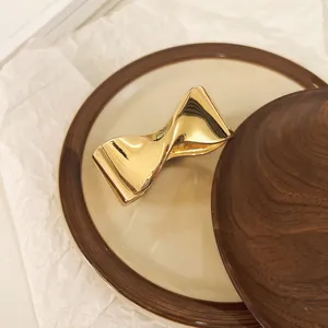 Vista detallada de un brazalete abierto retorcido geométrico dorado sobre un plato