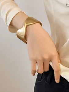 Primer plano detallado de un elegante brazalete geométrico ondulado en oro mate al brazo.