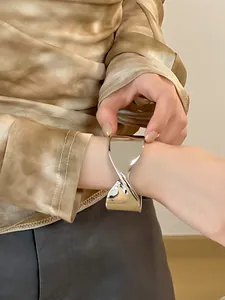 Primer plano de un brazalete abierto de metal plateado con diseño cruzado en la muñeca