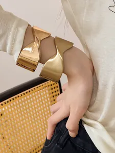 Detalle de brazaletes geométricos dorados retorcidos en acabados pulido y mate.