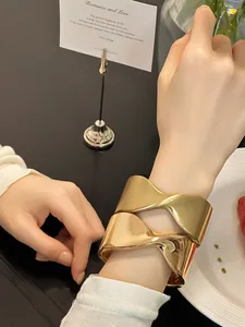 Primer plano de un brazalete de puño cruzado geométrico en oro mate en la muñeca