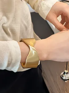 Primer plano de un brazalete de puño retorcido geométrico en oro mate en una muñeca