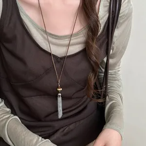 Detail shot of a long silver tassel necklace styled with a brown camisole and mesh top