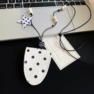 Detailed view of a stylish white polka dot leather glasses case pendant necklace on a desk
