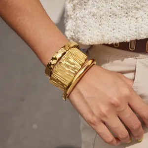 Primo piano di tre bracciali in acciaio al titanio dorato con diverse texture lavorate.