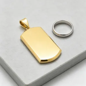 Close-up detail of blank gold dog tag pendant and silver ring on stone surface.