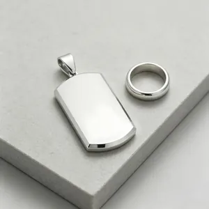 Close-up of blank silver dog tag pendant and plain steel ring on stone surface