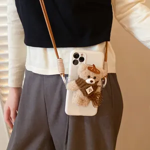 Close-up of plush bear charm with brown scarf and woven lanyard on white phone case