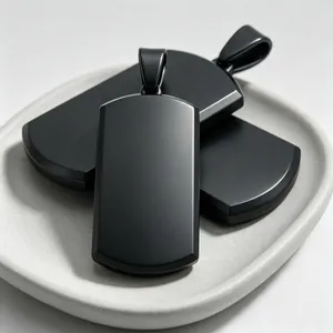 Close-up detail view of matte black titanium steel dog tag pendants on a ceramic tray